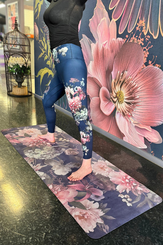 A person standing on a dark purple floral print yoga mat with large floral artwork in the background.