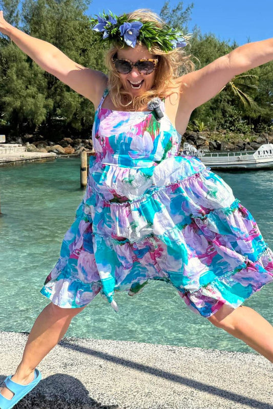 Woman in a colorful dress jumping by a waterfront with trees in the background
