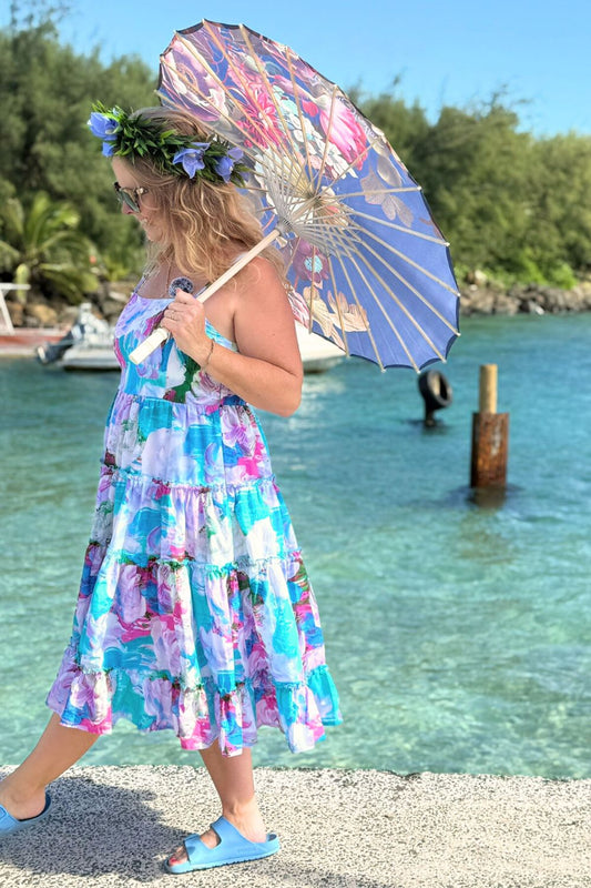 Woman in a colorful dress holding a floral umbrella by a waterfront