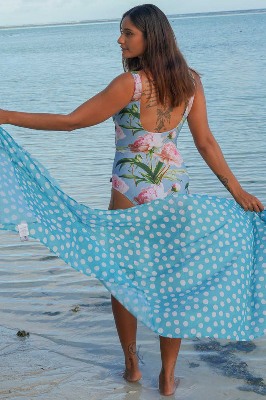 Woman in a floral swimsuit with a blue polka dot cover-up on a beach.