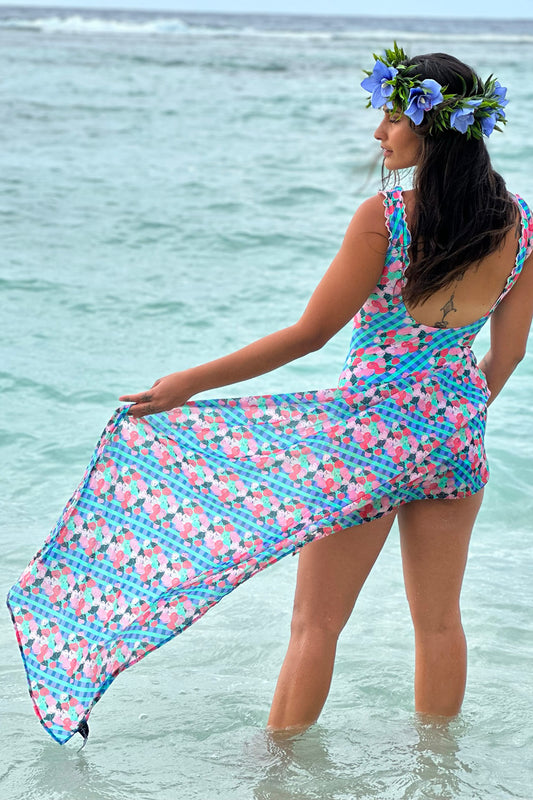 A person standing in shallow water by the beach, wearing a blue and pink checkered swim scarf wrap around their waist.
