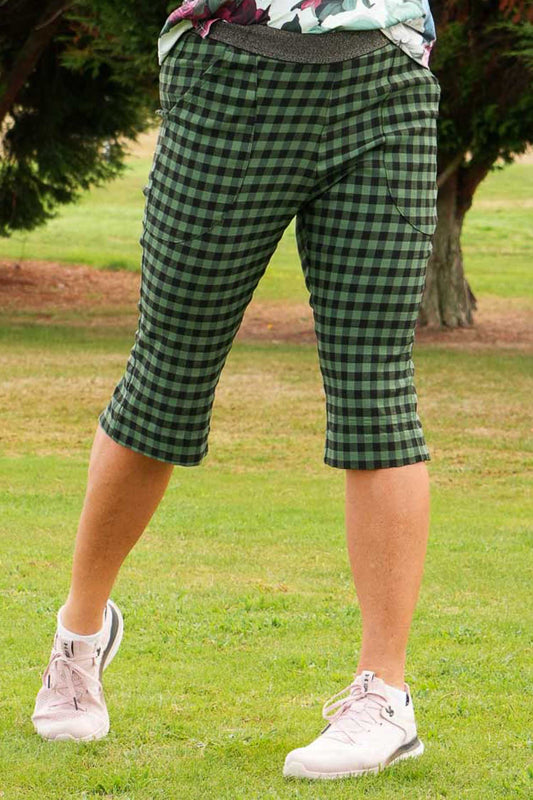 A pair of olive check capri pants worn by a person standing on a golf course, with a focus on the pants' fit and design.