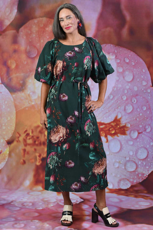 A model wearing a midi-length forest green dress with a floral print, featuring bell-shaped puff sleeves and a waist tie.