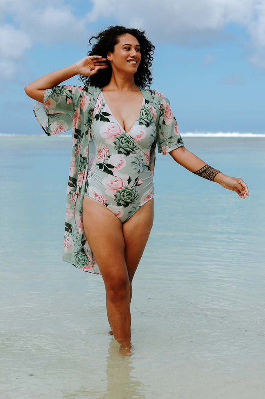 A woman standing in shallow water wearing a floral print one-piece swimsuit and a matching cover-up.