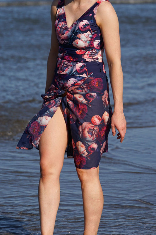 A person standing at the beach wearing a navy floral swim scarf wrap, which is also visible as a cover-up garment.