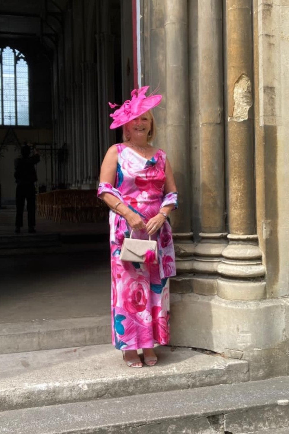 Woman in a pink floral dress and fascinator at a wedding 