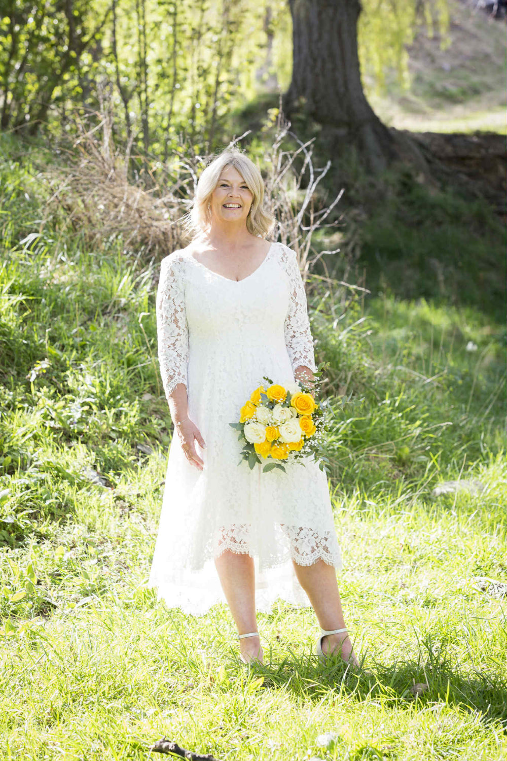 Woman in a white lace dress holding a bouquet of flowers in a grassy outdoor setting.
