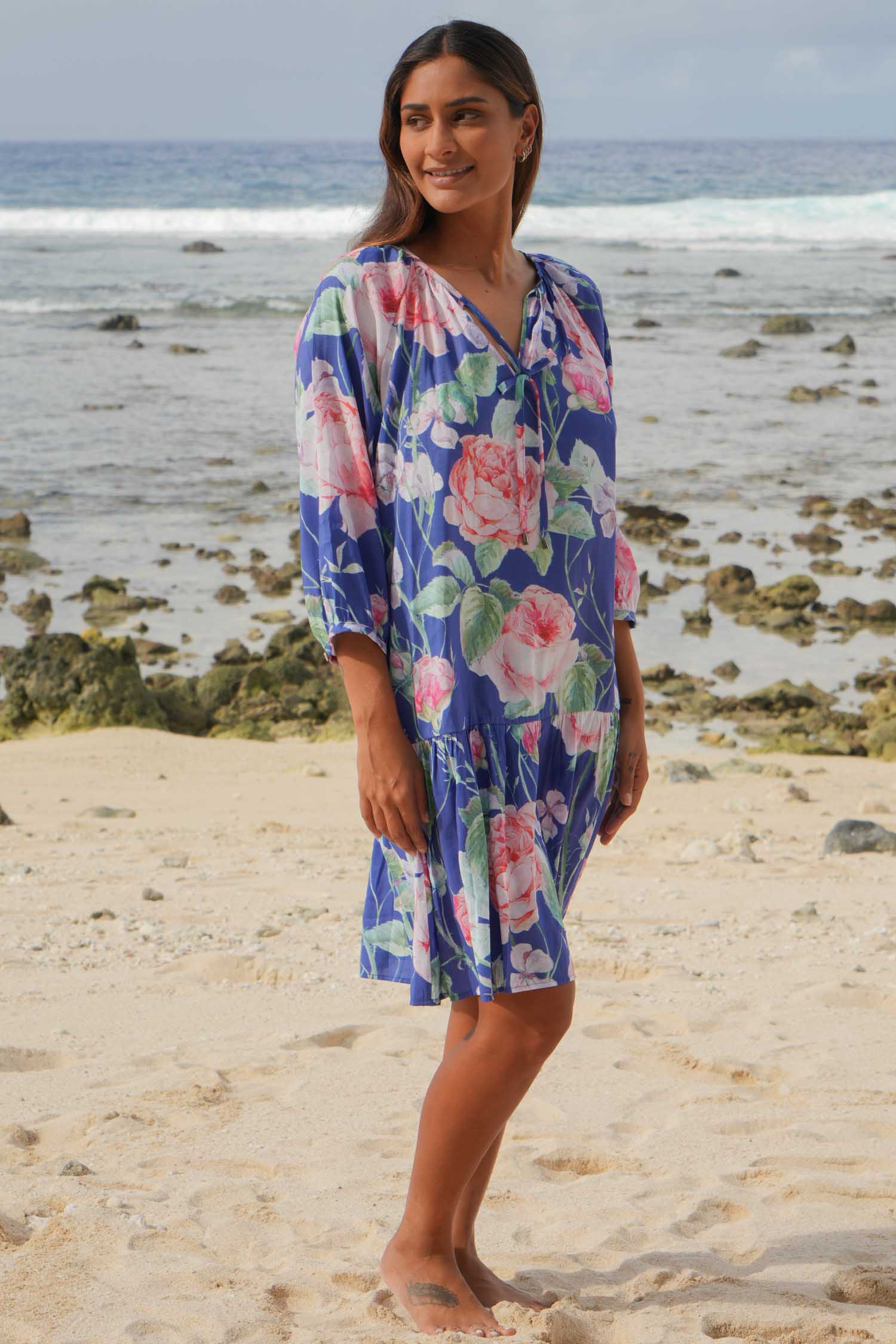 Woman wearing a floral dress on a beach with ocean in the background