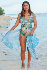 Woman in a floral swimsuit with a blue polka dot cover-up on a beach.