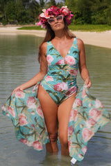 Woman in a floral swimsuit and cover-up standing in water with a tropical background