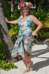 Woman in a floral bather standing on a sandy beach with palm trees in the background