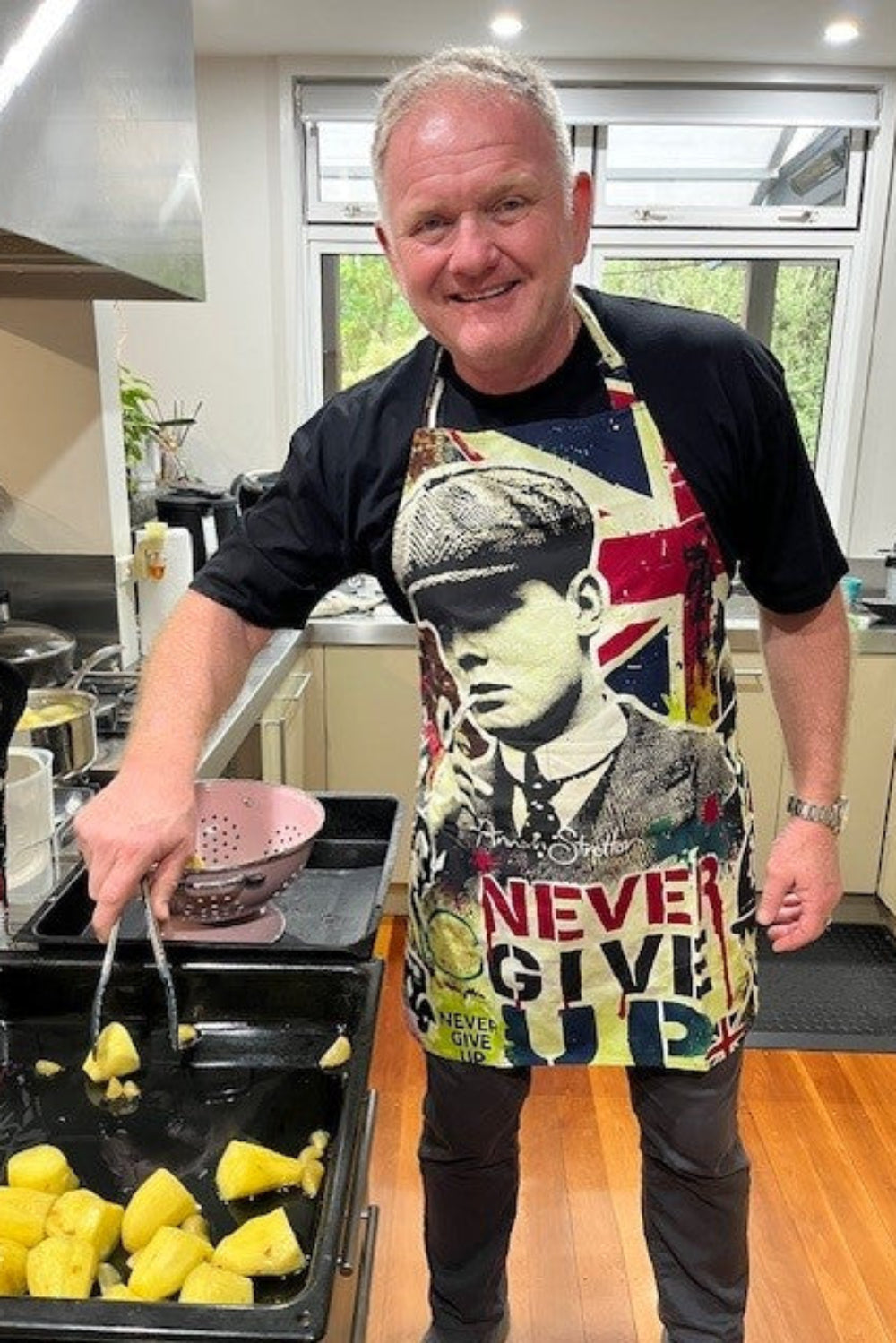 Man cooking in a kitchen wearing a colorful apron with a design and text.