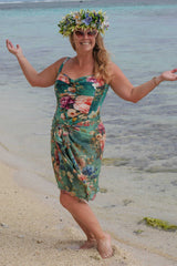 Woman in a floral dress and flower crown standing on a beach.