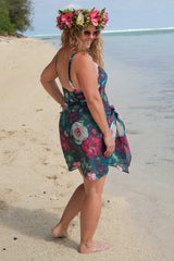 Woman in a floral dress and flower crown standing on a beach.