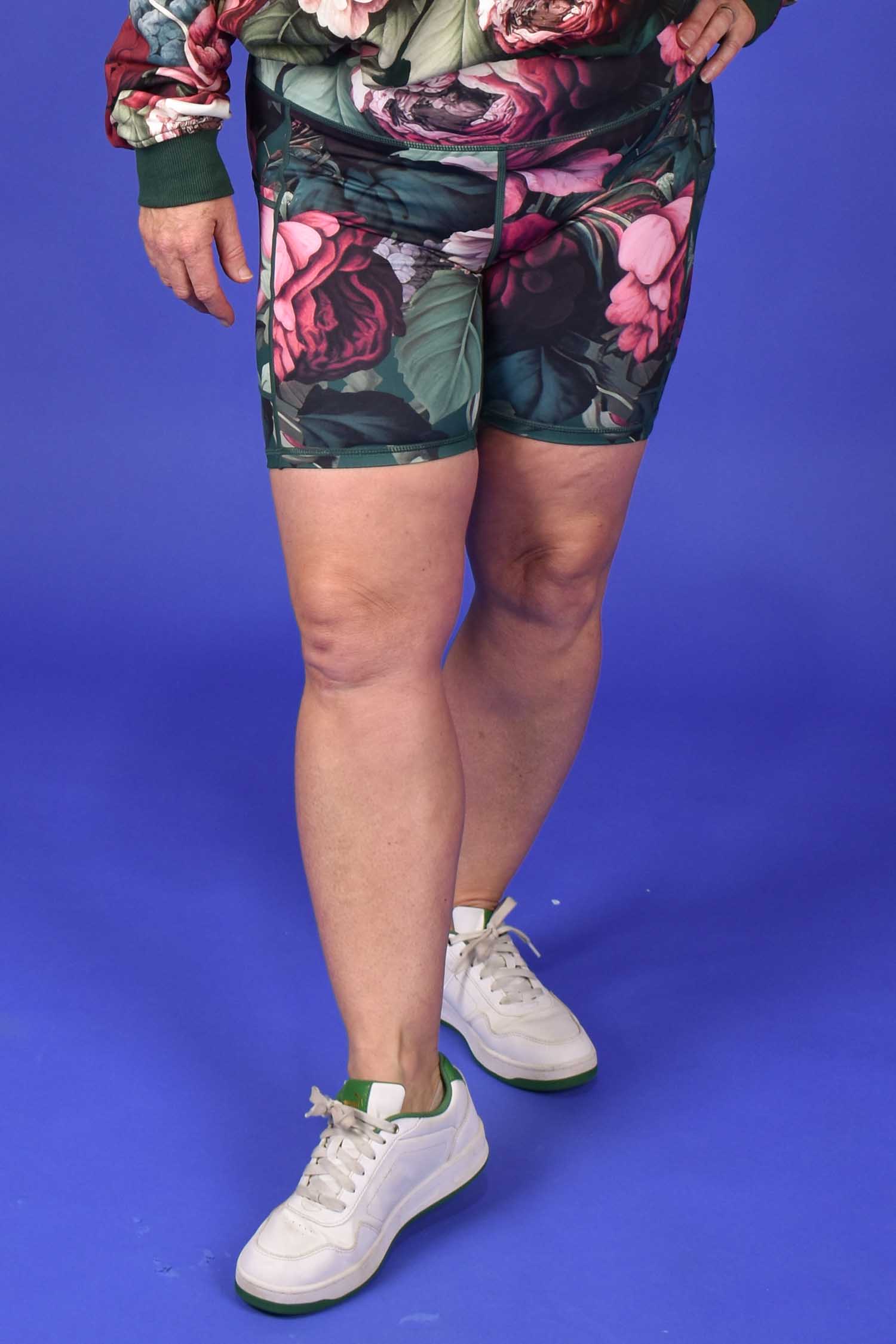 Person wearing floral shorts and white sneakers on a blue background