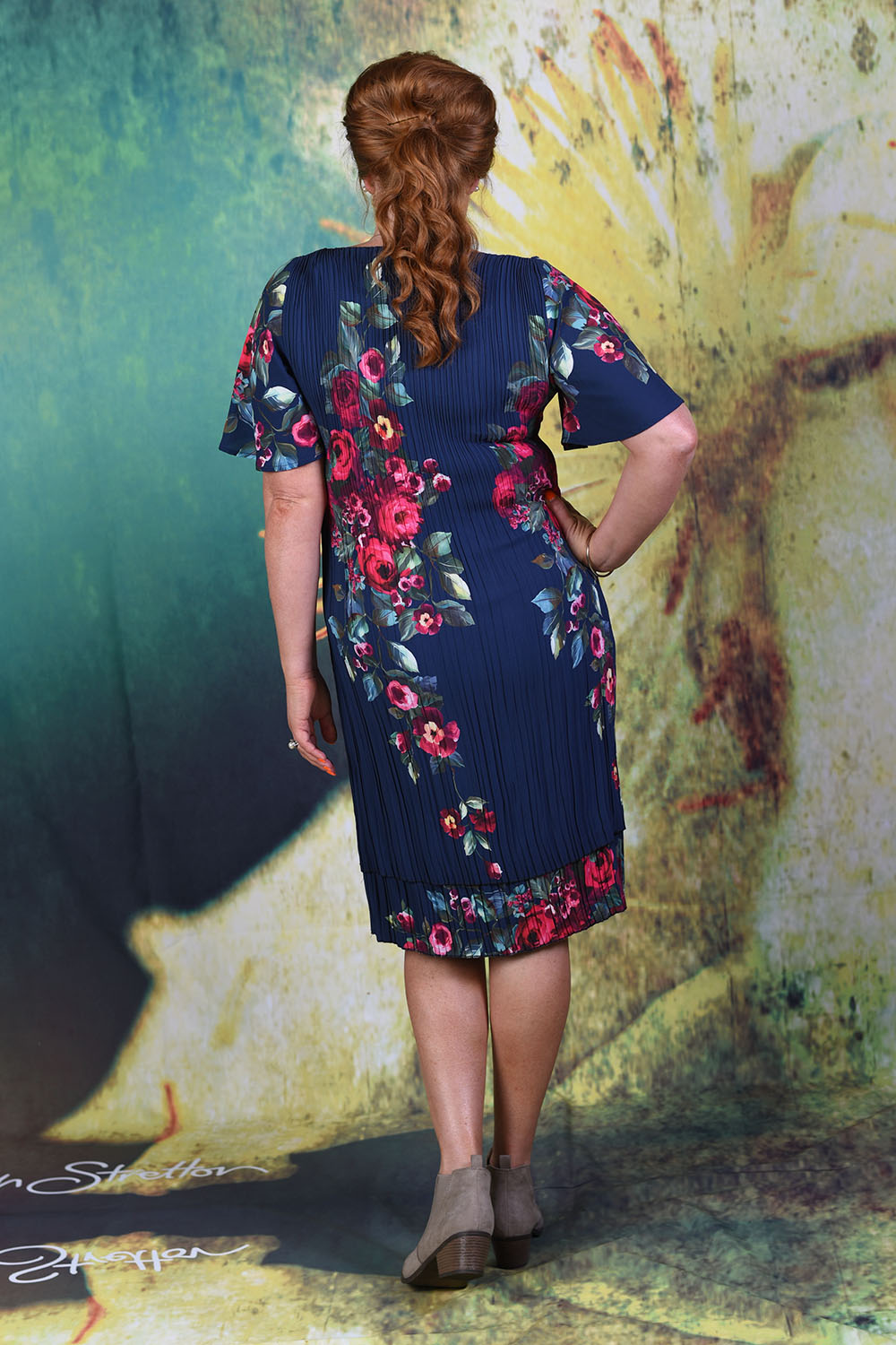 Back of second model wearing the Pleat Me Juliet dress in rose, with hand on hip.